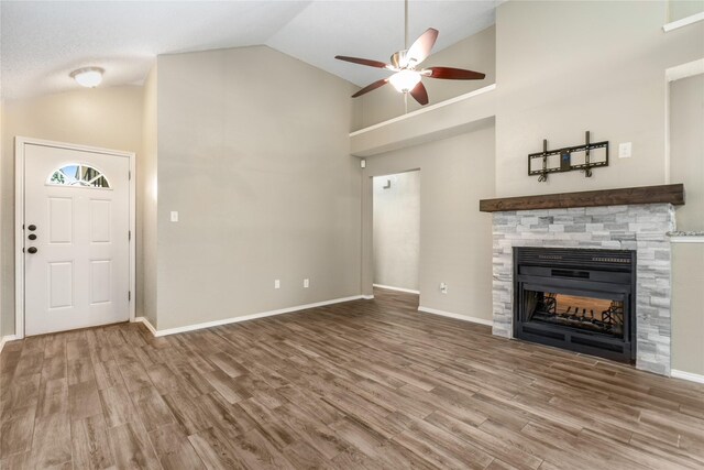 unfurnished living room featuring ceiling fan, a stone fireplace, wood finished floors, high vaulted ceiling, and baseboards