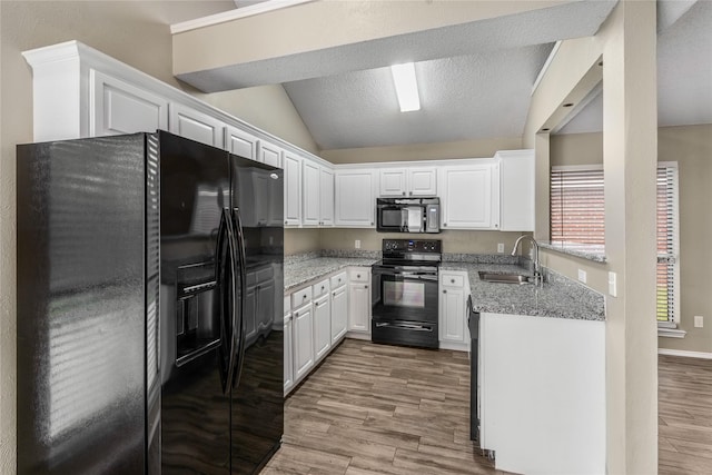 kitchen with vaulted ceiling, white cabinetry, a sink, black appliances, and light wood-style flooring