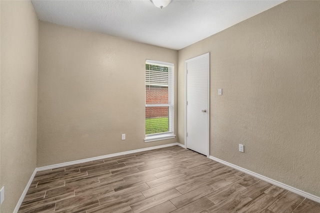 empty room with baseboards, a textured wall, and wood finished floors
