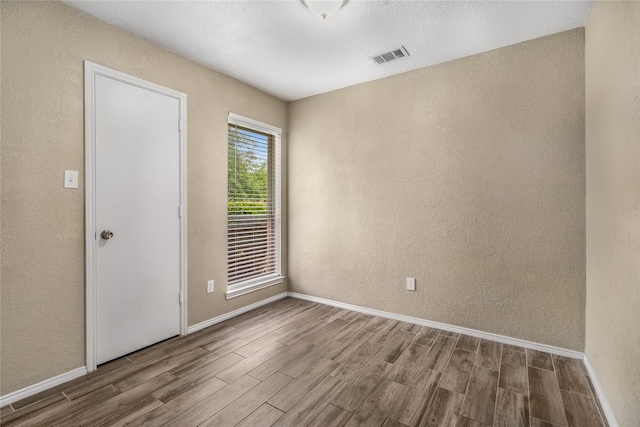 spare room featuring baseboards, a textured wall, wood finished floors, and visible vents