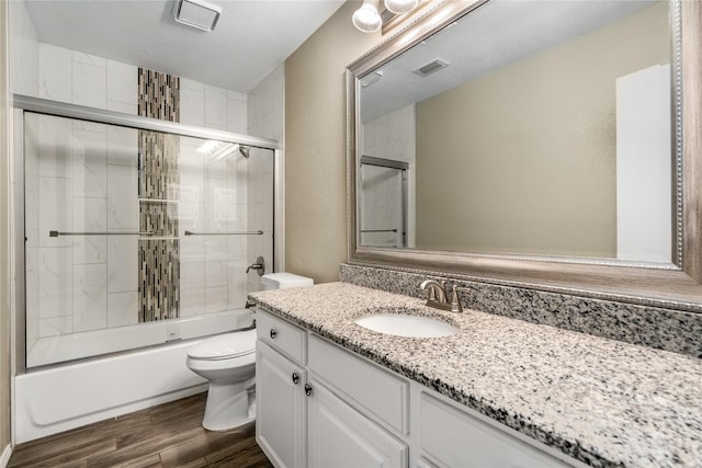 bathroom with shower / bath combination with glass door, vanity, toilet, wood finished floors, and visible vents