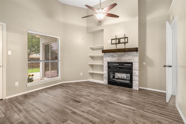 unfurnished living room featuring a ceiling fan, a fireplace, wood finished floors, baseboards, and a high ceiling