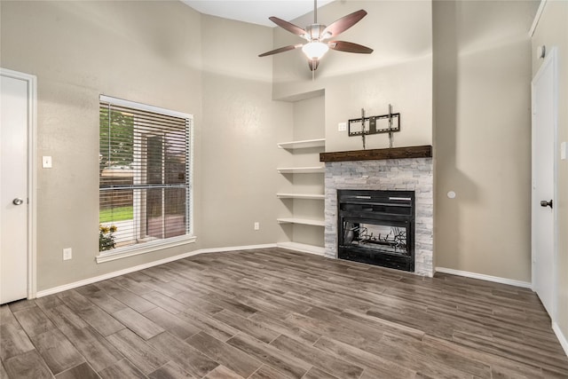unfurnished living room with a towering ceiling, wood finished floors, a fireplace, baseboards, and a ceiling fan