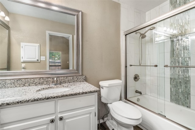 full bathroom with toilet, a textured wall, bath / shower combo with glass door, and vanity