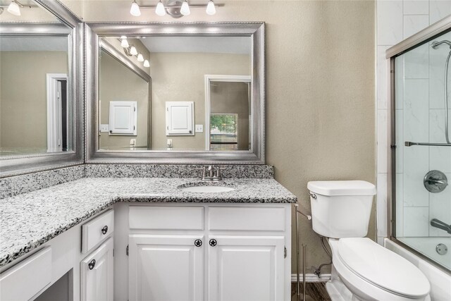 full bath with vanity, a textured wall, combined bath / shower with glass door, and toilet