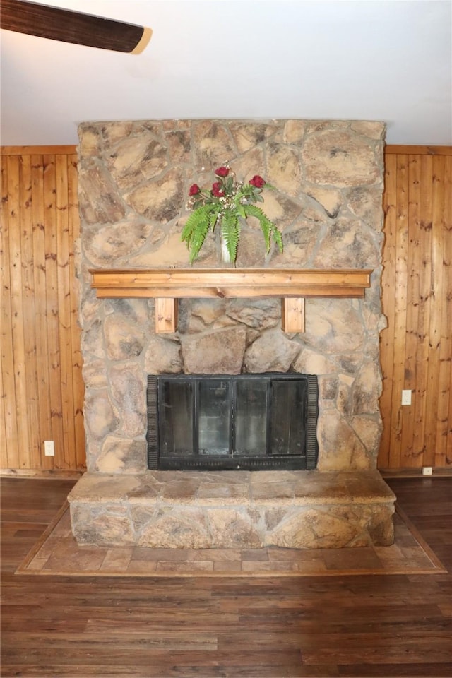 interior details with wooden walls, baseboards, a stone fireplace, and wood finished floors