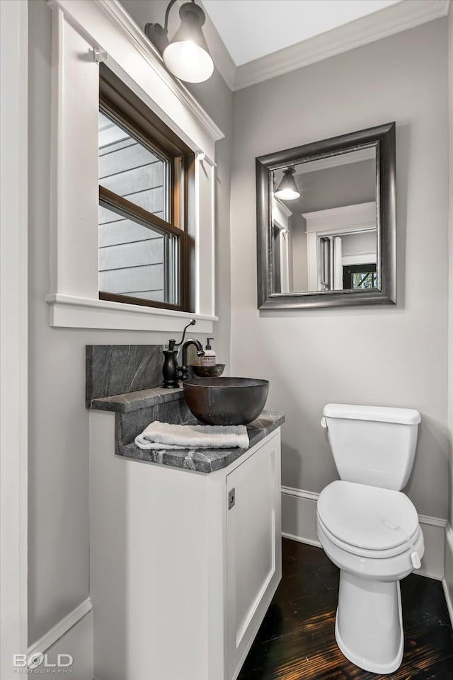 half bath with wood finished floors, baseboards, vanity, toilet, and ornamental molding