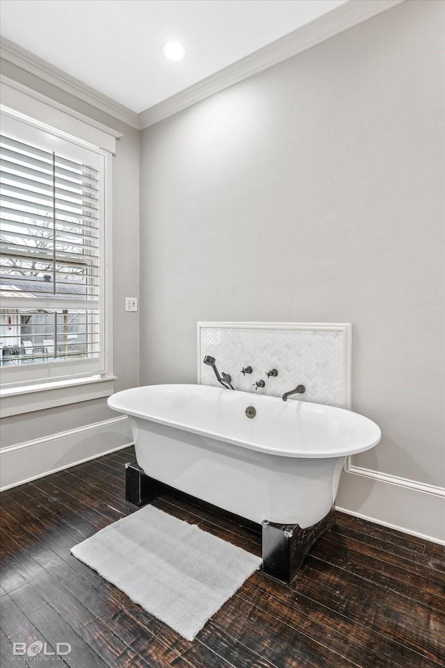 bathroom with crown molding, baseboards, hardwood / wood-style floors, and a soaking tub