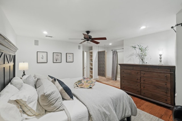 bedroom with ceiling fan, a barn door, recessed lighting, wood finished floors, and visible vents