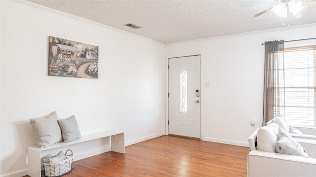 foyer featuring light wood finished floors, a textured ceiling, a ceiling fan, visible vents, and ornamental molding