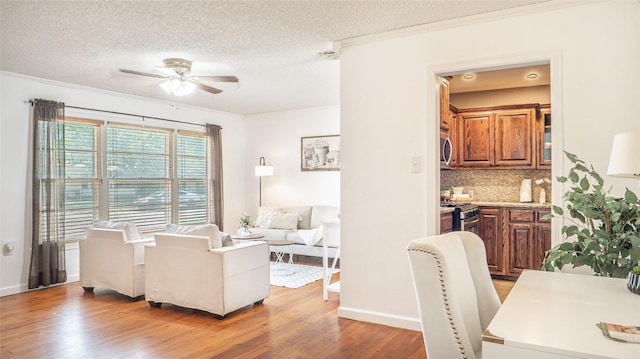 living room with a textured ceiling, ceiling fan, ornamental molding, and light wood-style flooring