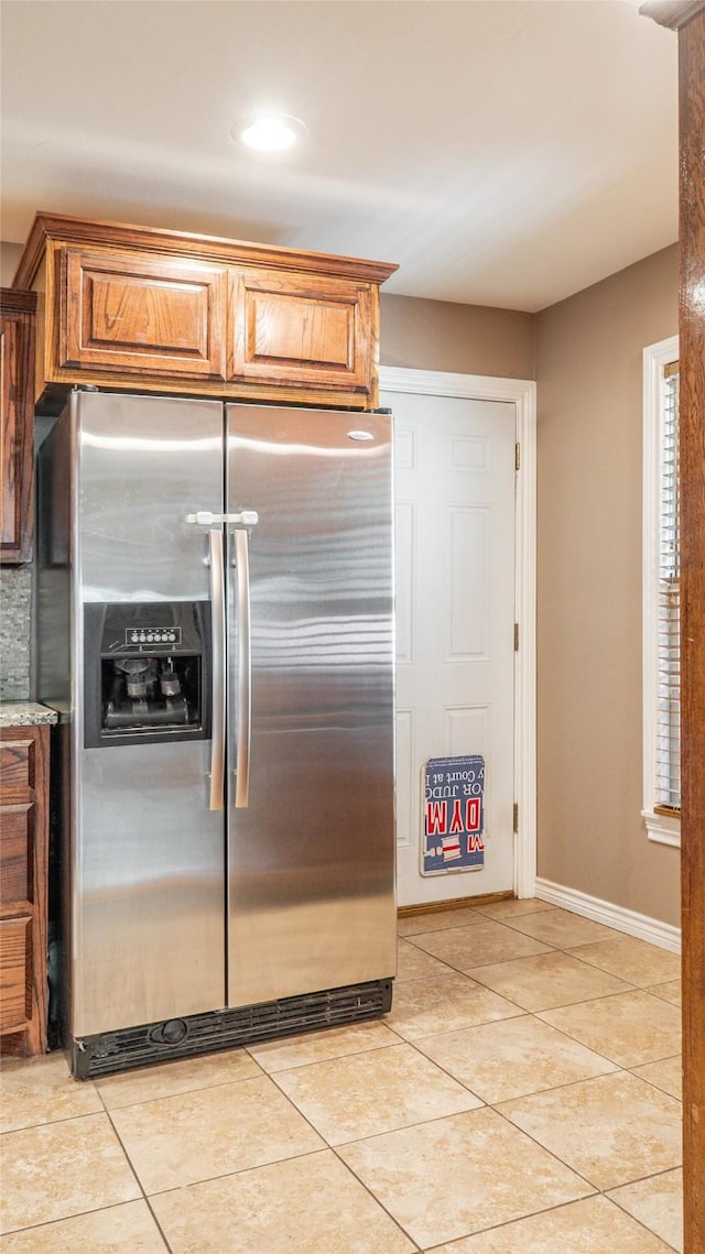 kitchen with stainless steel refrigerator with ice dispenser, baseboards, light tile patterned floors, and brown cabinets