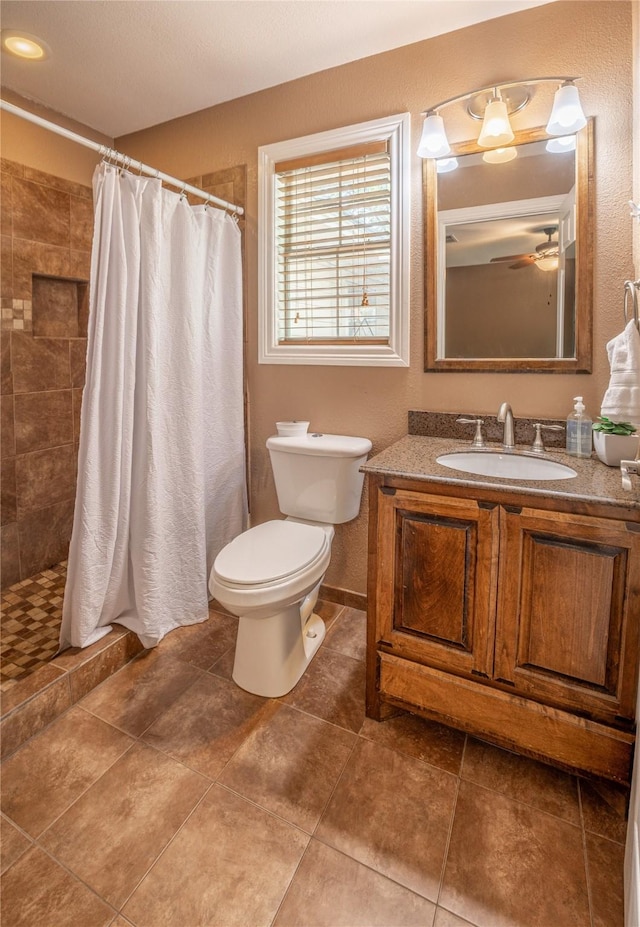 bathroom with vanity, ceiling fan, toilet, and tiled shower