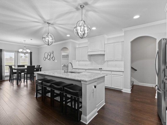 kitchen with black electric cooktop, arched walkways, a chandelier, custom range hood, and a sink