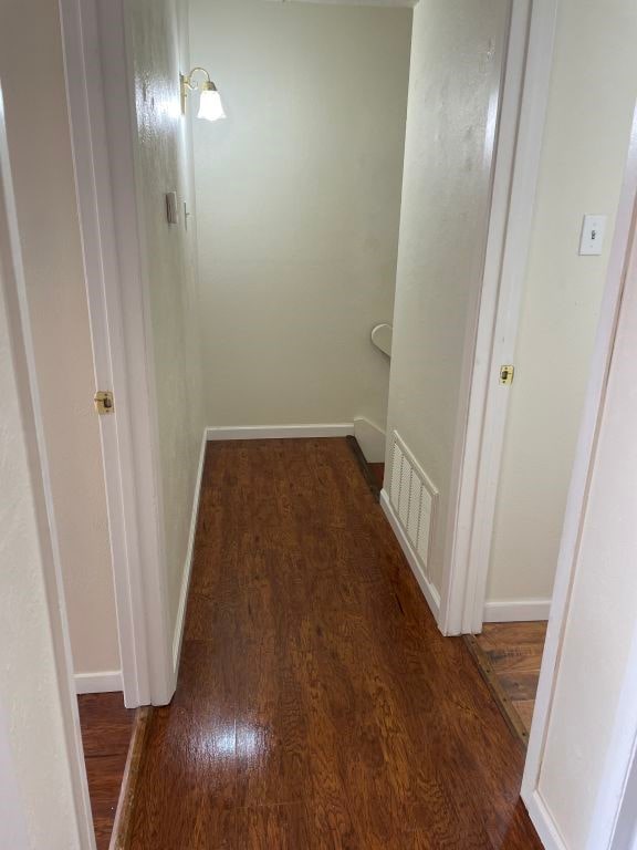 hall featuring baseboards, wood finished floors, and visible vents