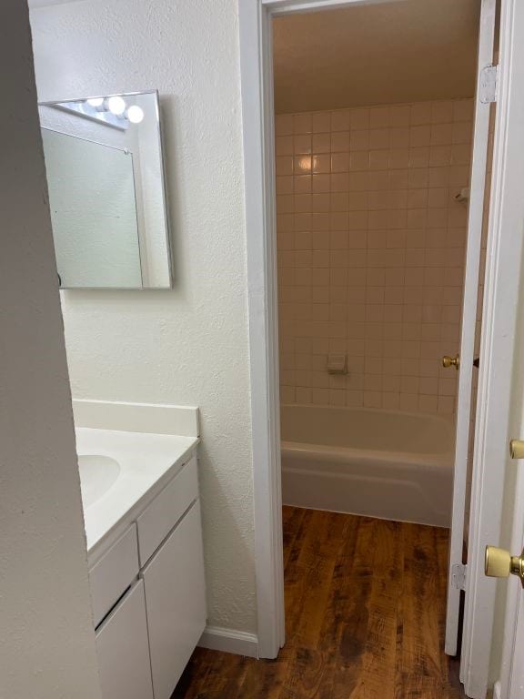 full bath featuring vanity, a textured wall, shower / tub combination, and wood finished floors