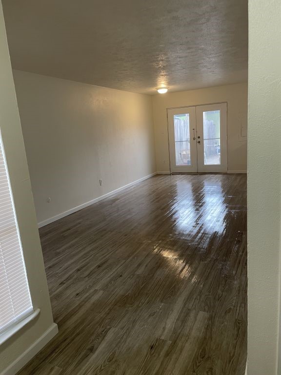 spare room featuring french doors, a textured ceiling, baseboards, and dark wood-style floors