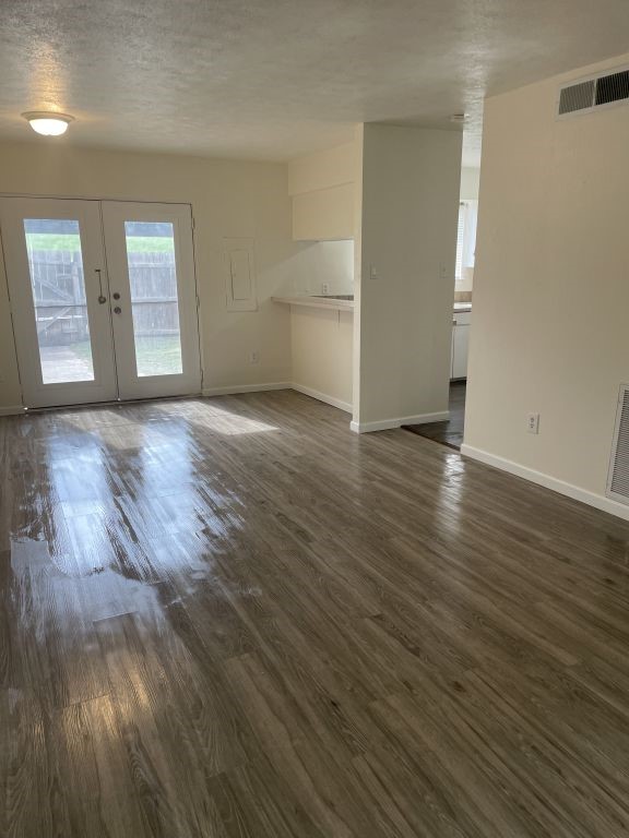 unfurnished living room with a textured ceiling, french doors, baseboards, visible vents, and dark wood-style floors