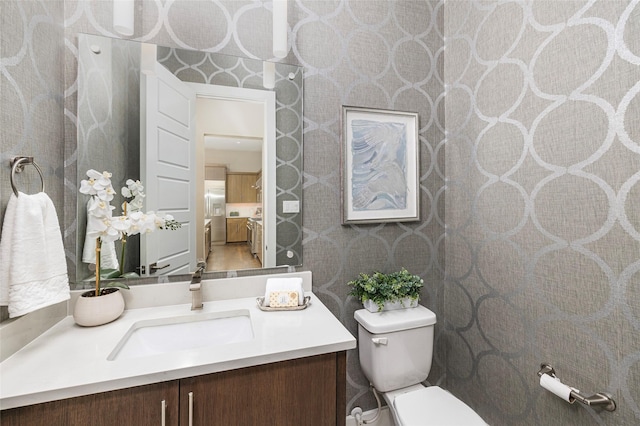 bathroom with vanity, wallpapered walls, and toilet