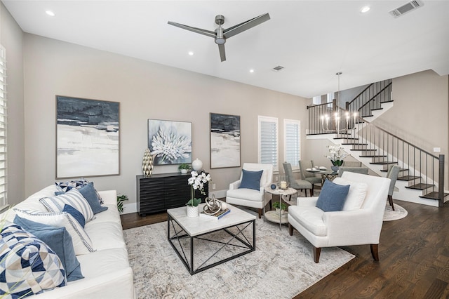 living area featuring visible vents, stairs, ceiling fan with notable chandelier, and wood finished floors
