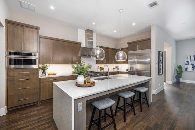 kitchen with wall chimney range hood, stainless steel appliances, dark wood-type flooring, and visible vents