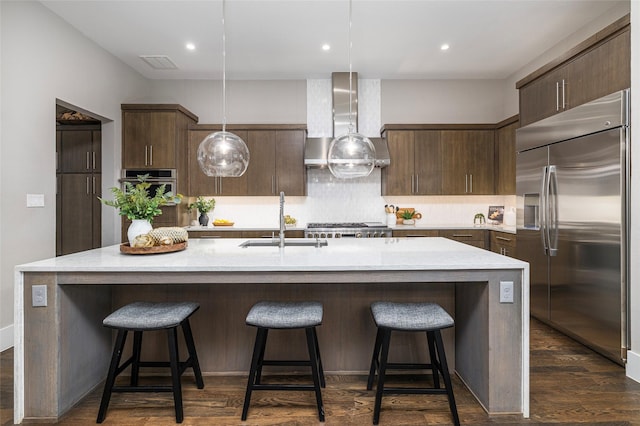 kitchen with wall chimney range hood, a sink, stainless steel appliances, decorative backsplash, and dark wood-style floors