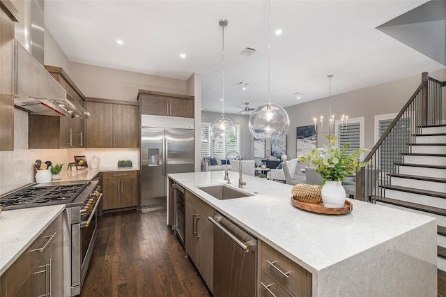 kitchen featuring dark wood-style flooring, a sink, wall chimney exhaust hood, a large island with sink, and premium appliances