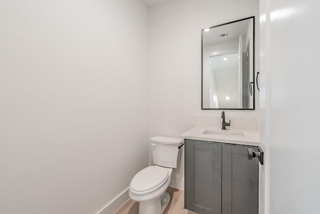 half bathroom with visible vents, wood finished floors, vanity, baseboards, and toilet