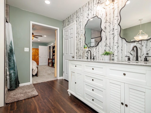 ensuite bathroom featuring double vanity, a ceiling fan, wood finished floors, a sink, and baseboards