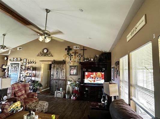 living room featuring ceiling fan, visible vents, a barn door, wood finished floors, and lofted ceiling