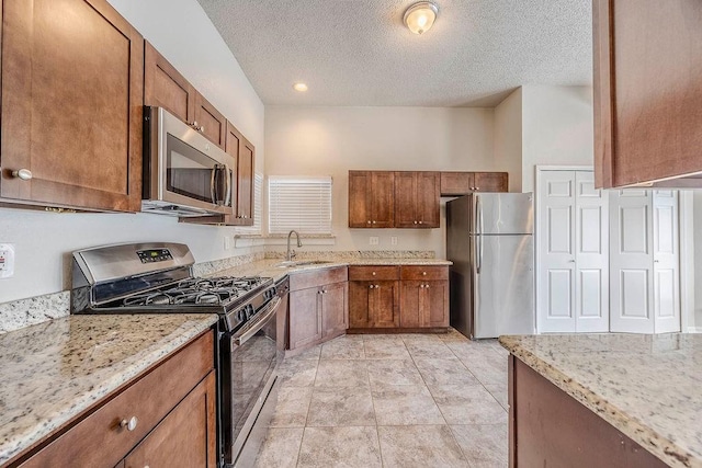 kitchen with light stone countertops, a textured ceiling, brown cabinets, a sink, and stainless steel appliances