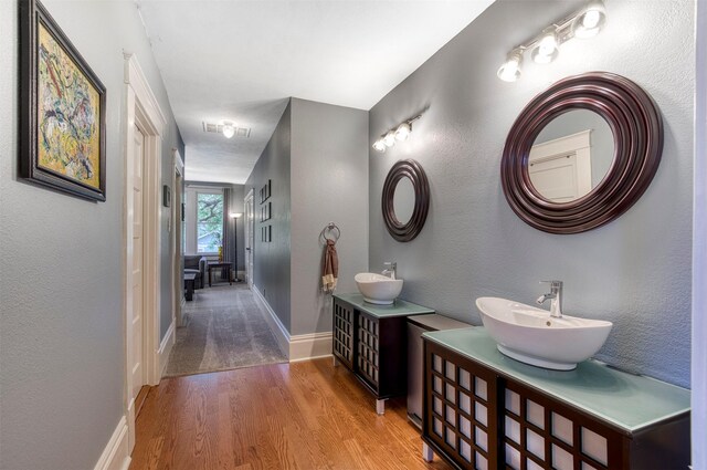 full bath featuring a sink, baseboards, wood finished floors, and two vanities