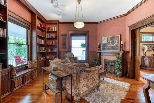 interior space with a fireplace with flush hearth, ornamental molding, wood finished floors, and a wainscoted wall