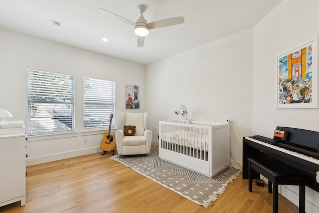 bedroom featuring a nursery area, baseboards, ceiling fan, and wood finished floors
