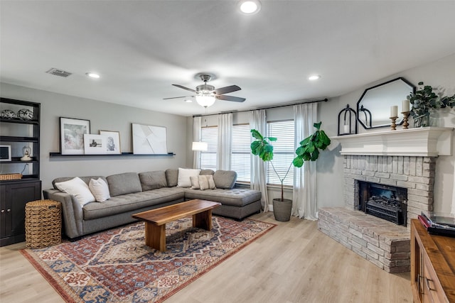 living room with light wood finished floors, a brick fireplace, a ceiling fan, recessed lighting, and visible vents