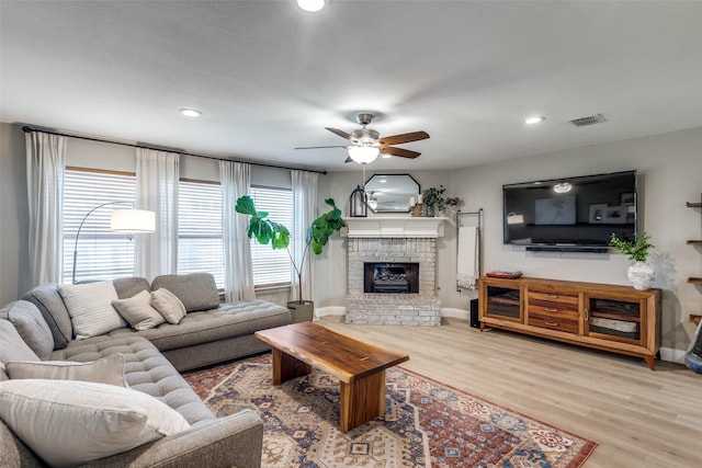 living room featuring ceiling fan, a fireplace, baseboards, wood finished floors, and visible vents