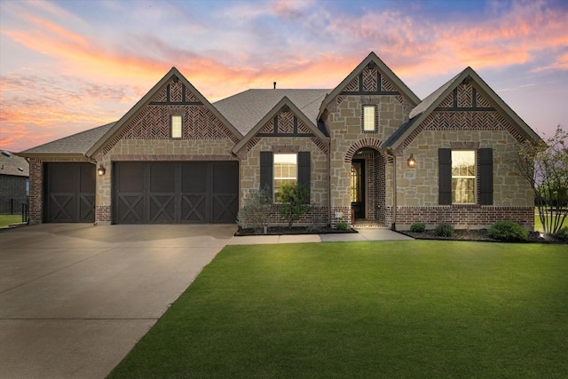 french provincial home featuring a garage, stone siding, brick siding, concrete driveway, and a lawn