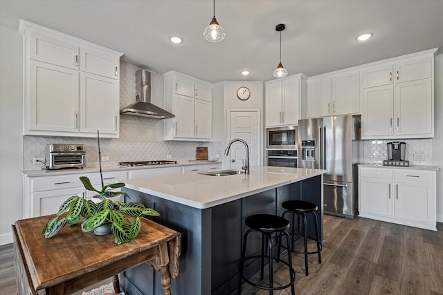 kitchen with dark wood-style flooring, a sink, wall chimney exhaust hood, stainless steel appliances, and white cabinetry