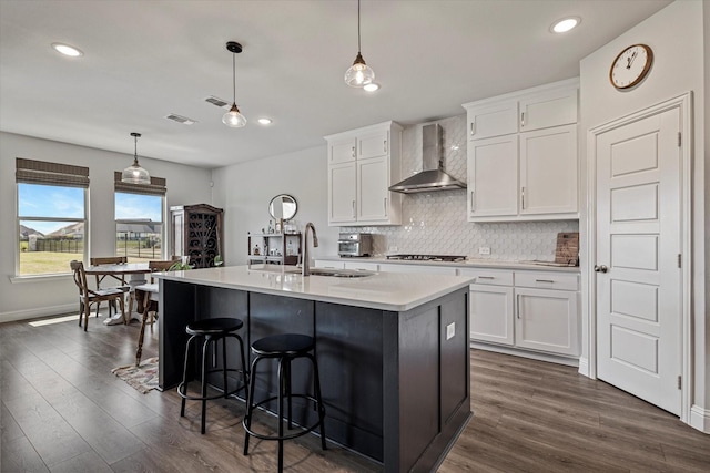 kitchen with wall chimney range hood, visible vents, dark wood-style floors, and stainless steel gas stovetop