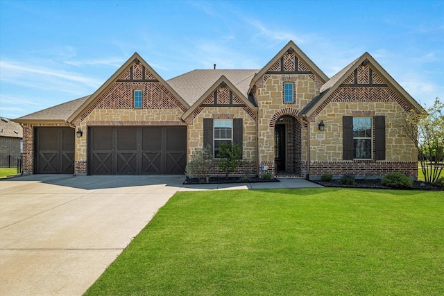 view of front of house with an attached garage, a shingled roof, stone siding, a front yard, and concrete driveway
