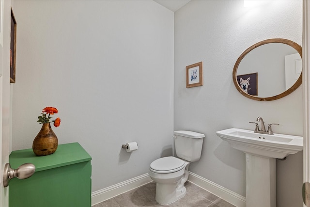 half bathroom with toilet, baseboards, and a sink