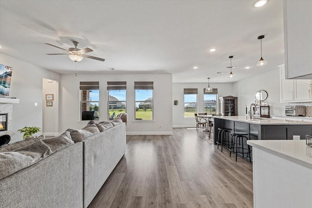 living room featuring dark wood-style flooring, a glass covered fireplace, a ceiling fan, recessed lighting, and baseboards