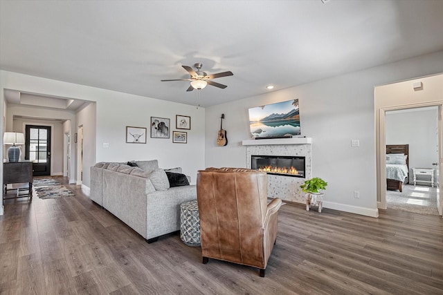 living area featuring a glass covered fireplace, baseboards, ceiling fan, and dark wood-type flooring