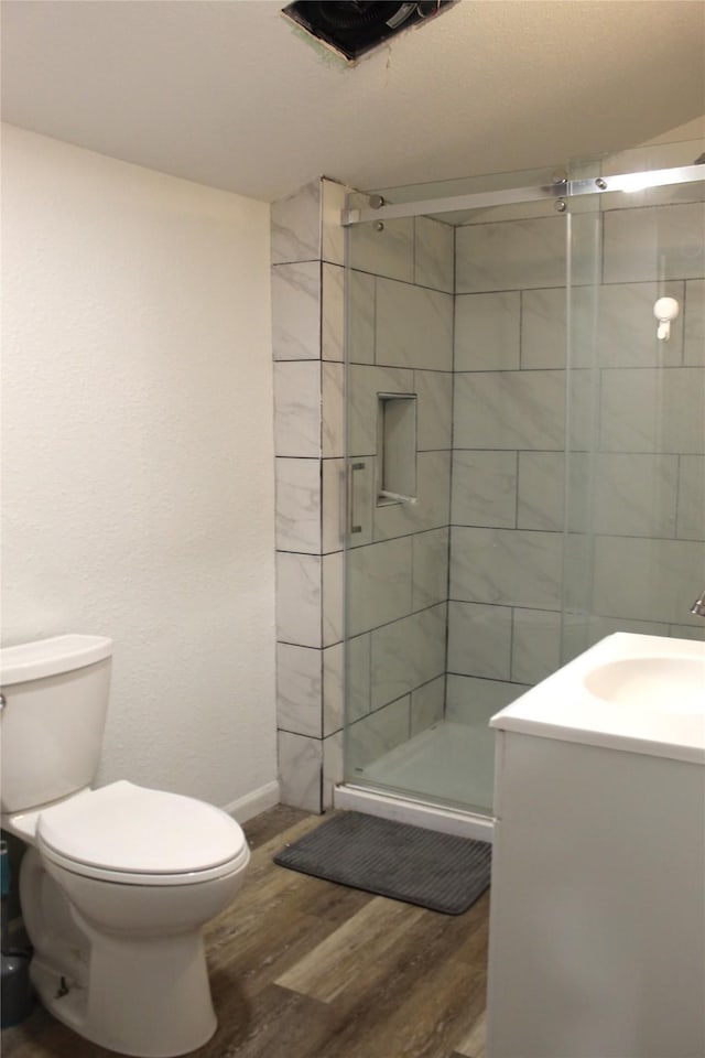 full bathroom featuring a shower stall, wood finished floors, vanity, baseboards, and toilet