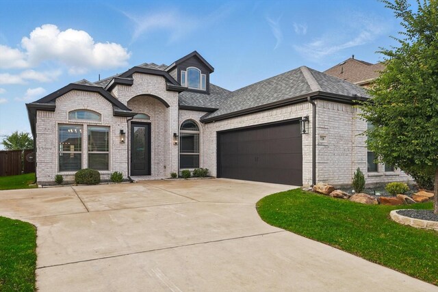french country style house featuring driveway, brick siding, fence, a garage, and roof with shingles