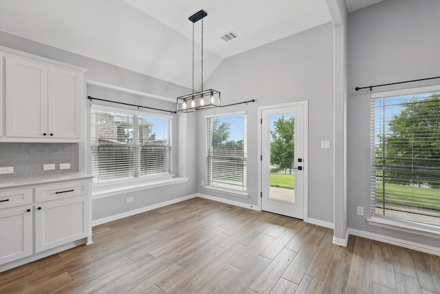 unfurnished dining area featuring vaulted ceiling, plenty of natural light, baseboards, and visible vents