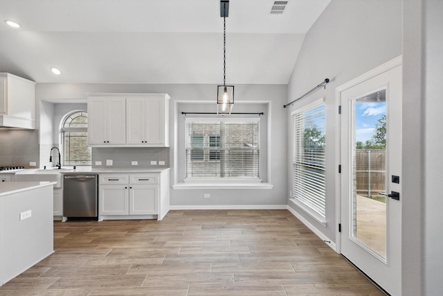 kitchen with vaulted ceiling, stainless steel dishwasher, white cabinetry, and light countertops