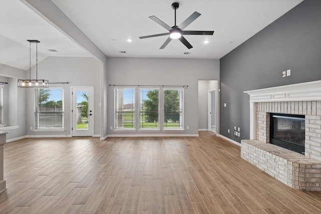 unfurnished living room featuring plenty of natural light, vaulted ceiling, ceiling fan with notable chandelier, and light wood-type flooring