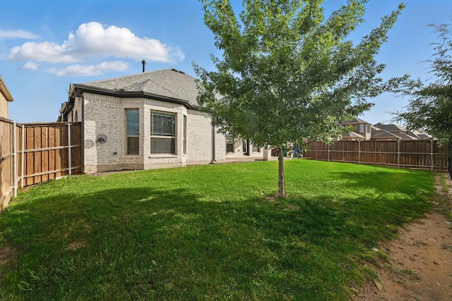 rear view of property featuring brick siding, roof with shingles, a lawn, and a fenced backyard