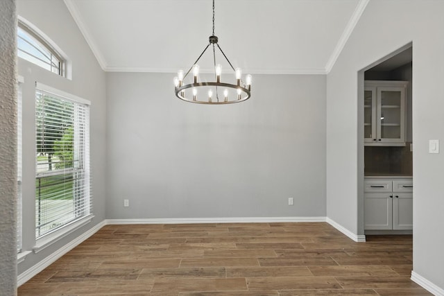 unfurnished dining area featuring a chandelier, ornamental molding, baseboards, and wood finished floors